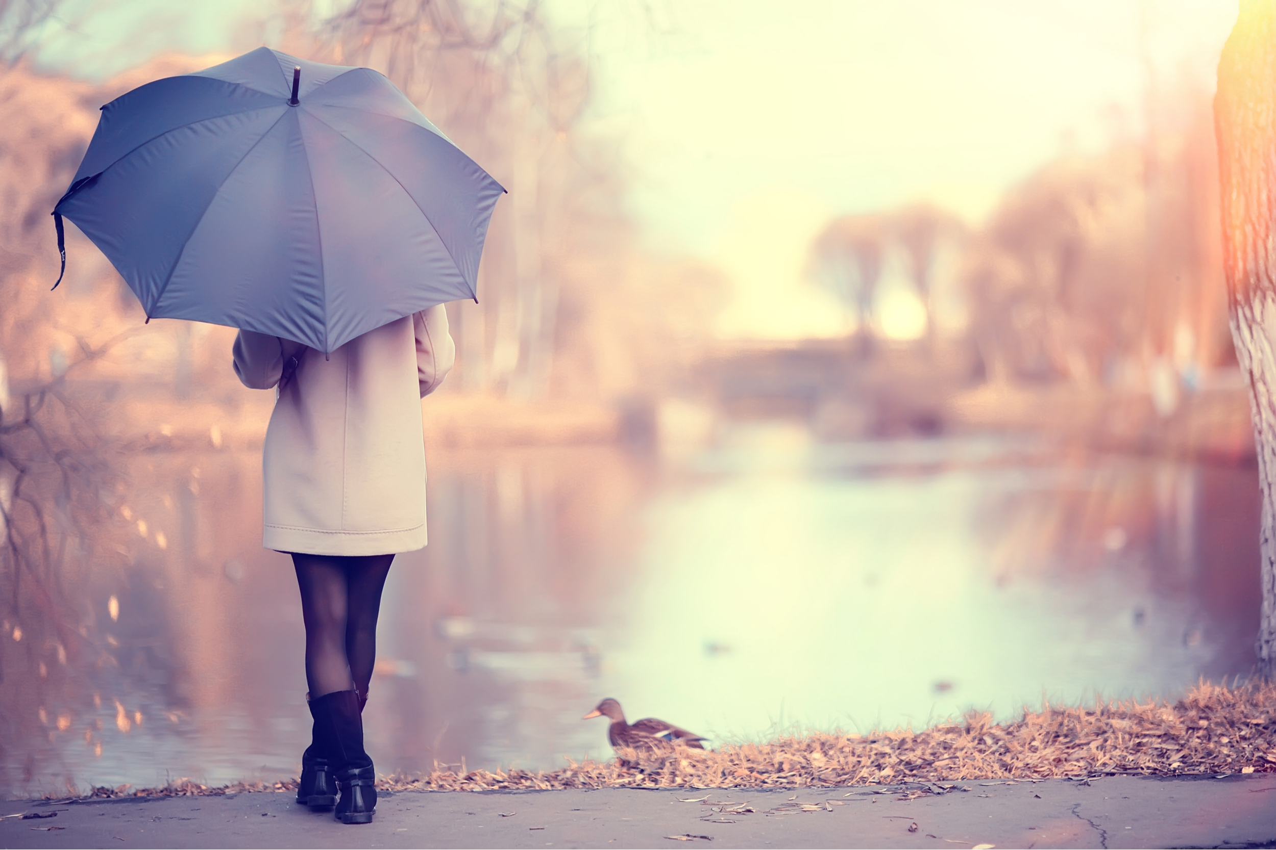 A woman standing under an umbrella at the side of a lake.