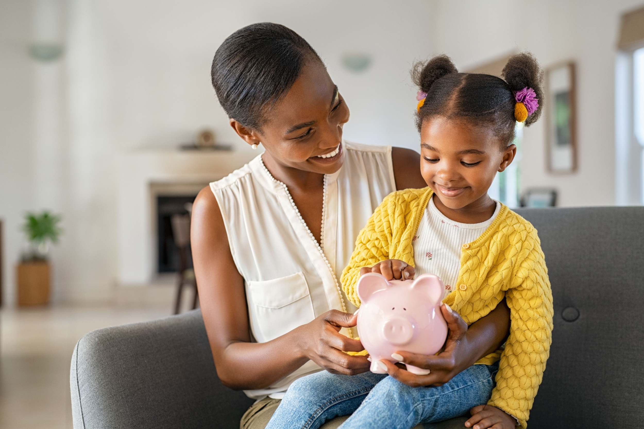 A woman with her child on her knee holding a piggy bank.