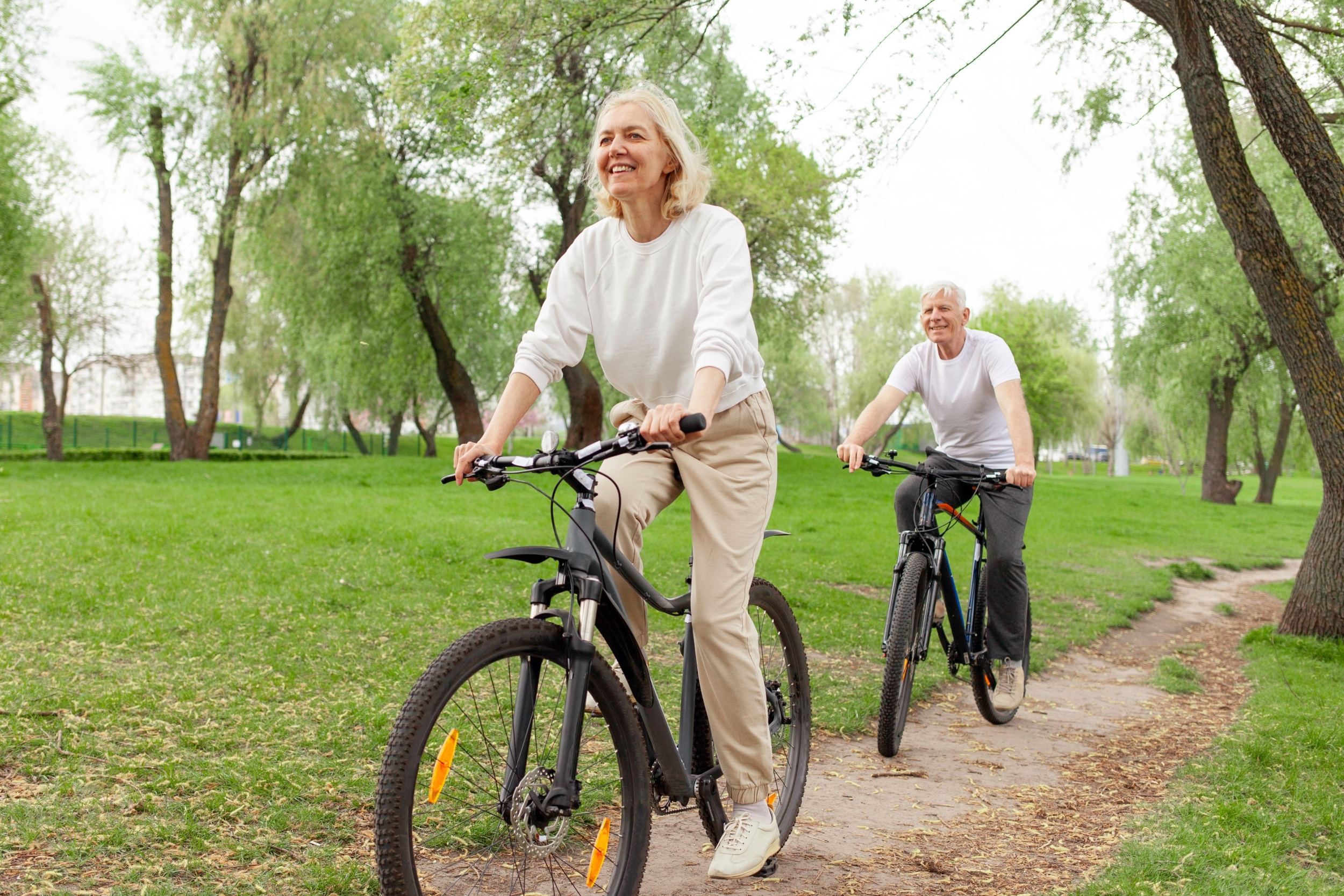 An elderly couple riding their bikes in the park.