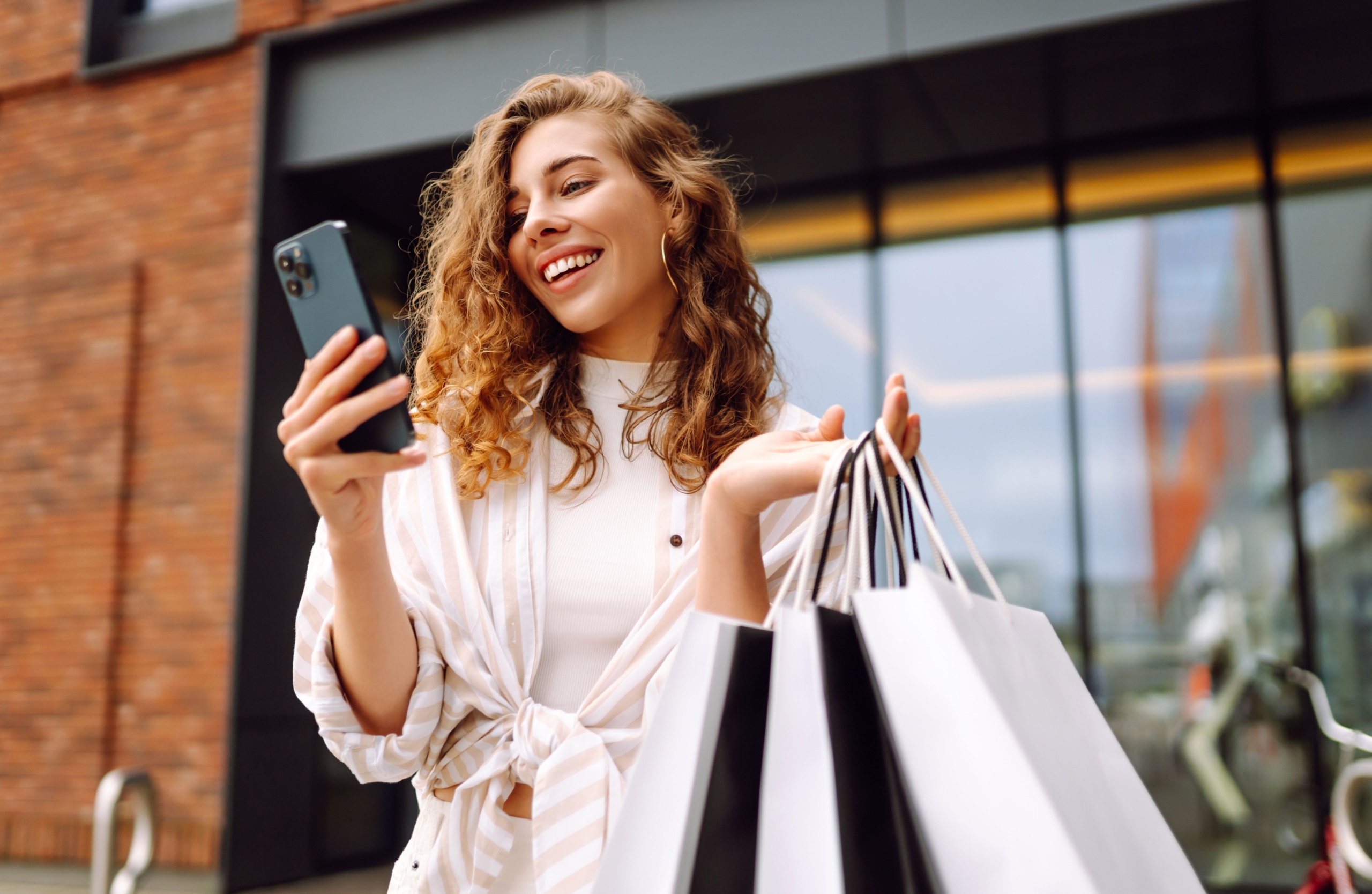 A woman holding shopping bags while on her phone.