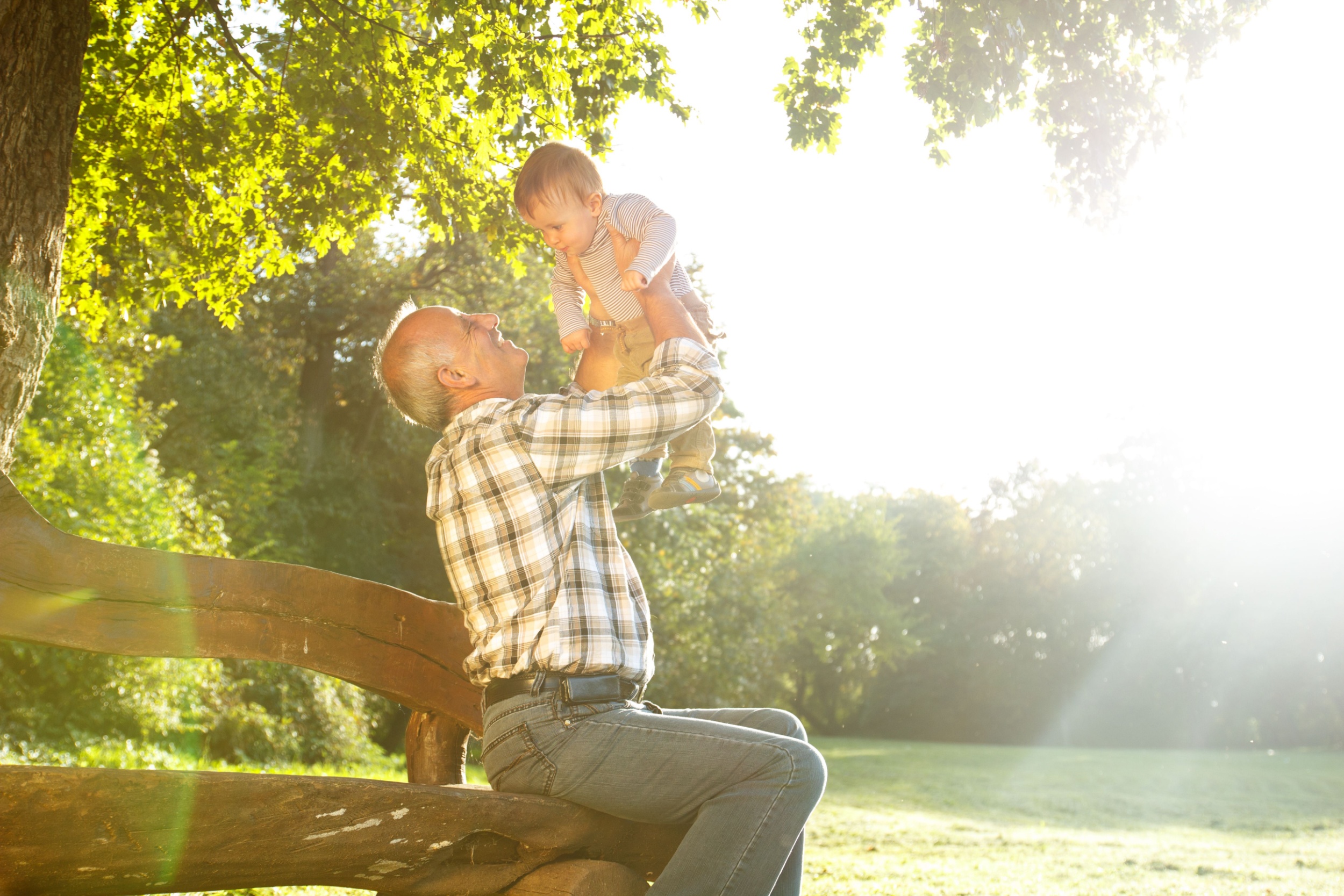A grandfather playing with his young grandson in a park.