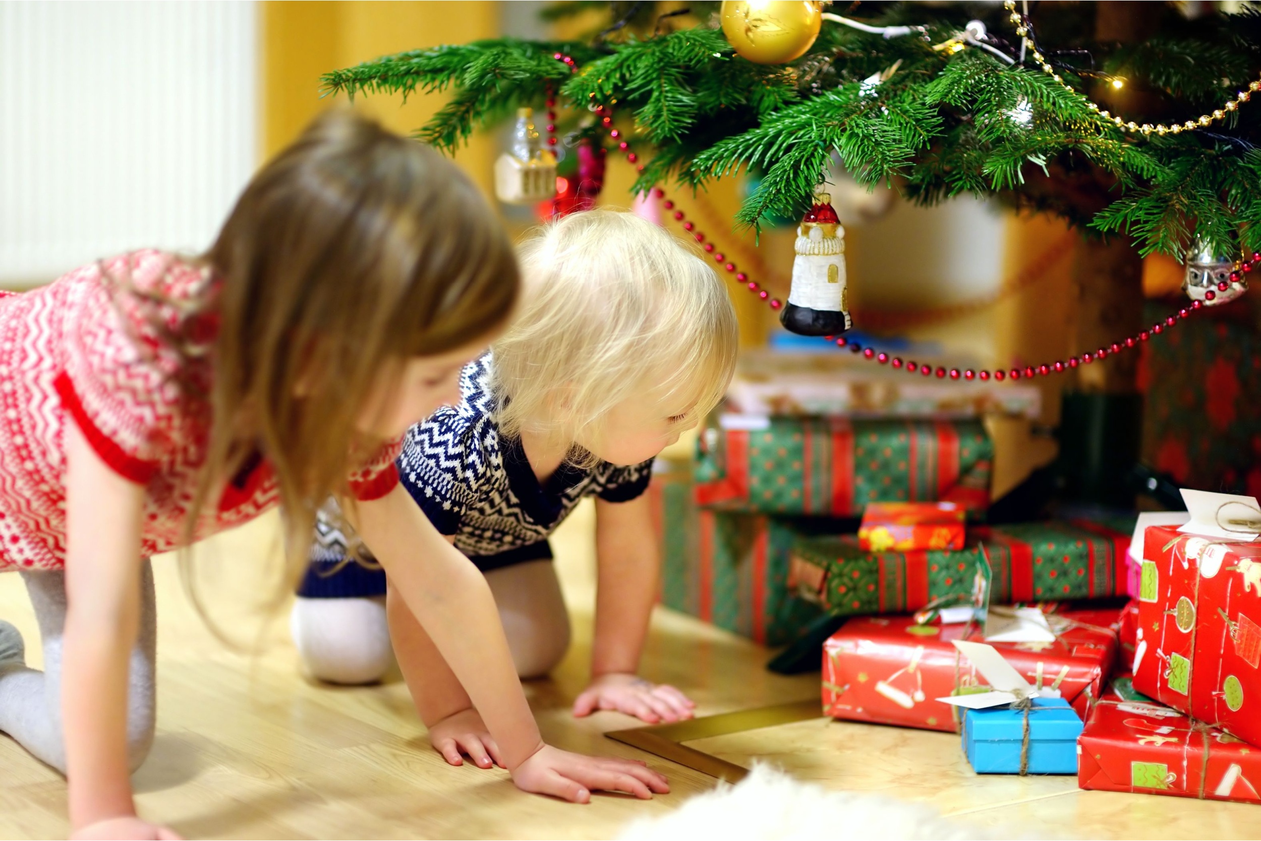 Two children looking at Christmas presents under a tree.
