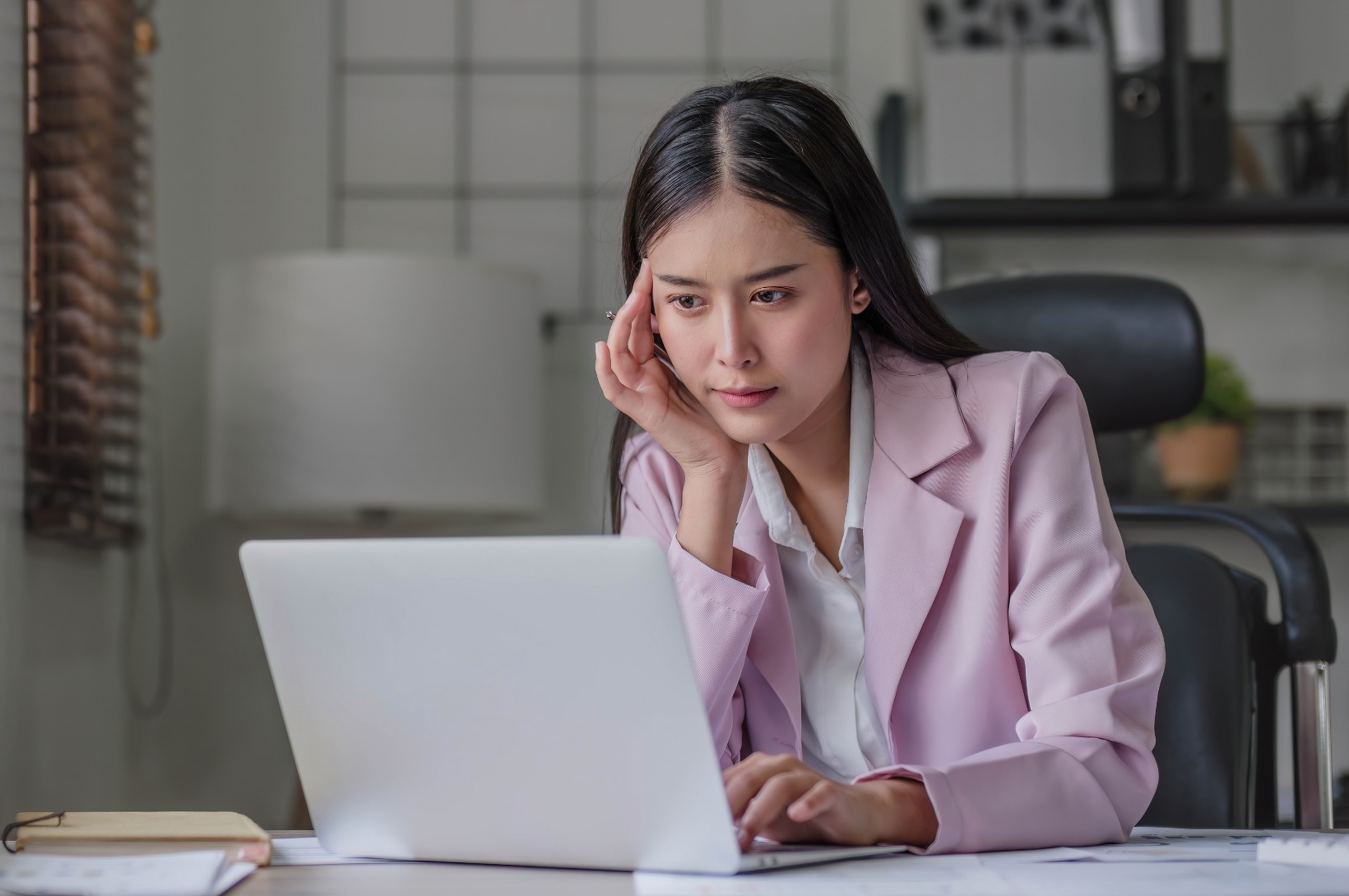 A woman at her computer, thinking carefully.